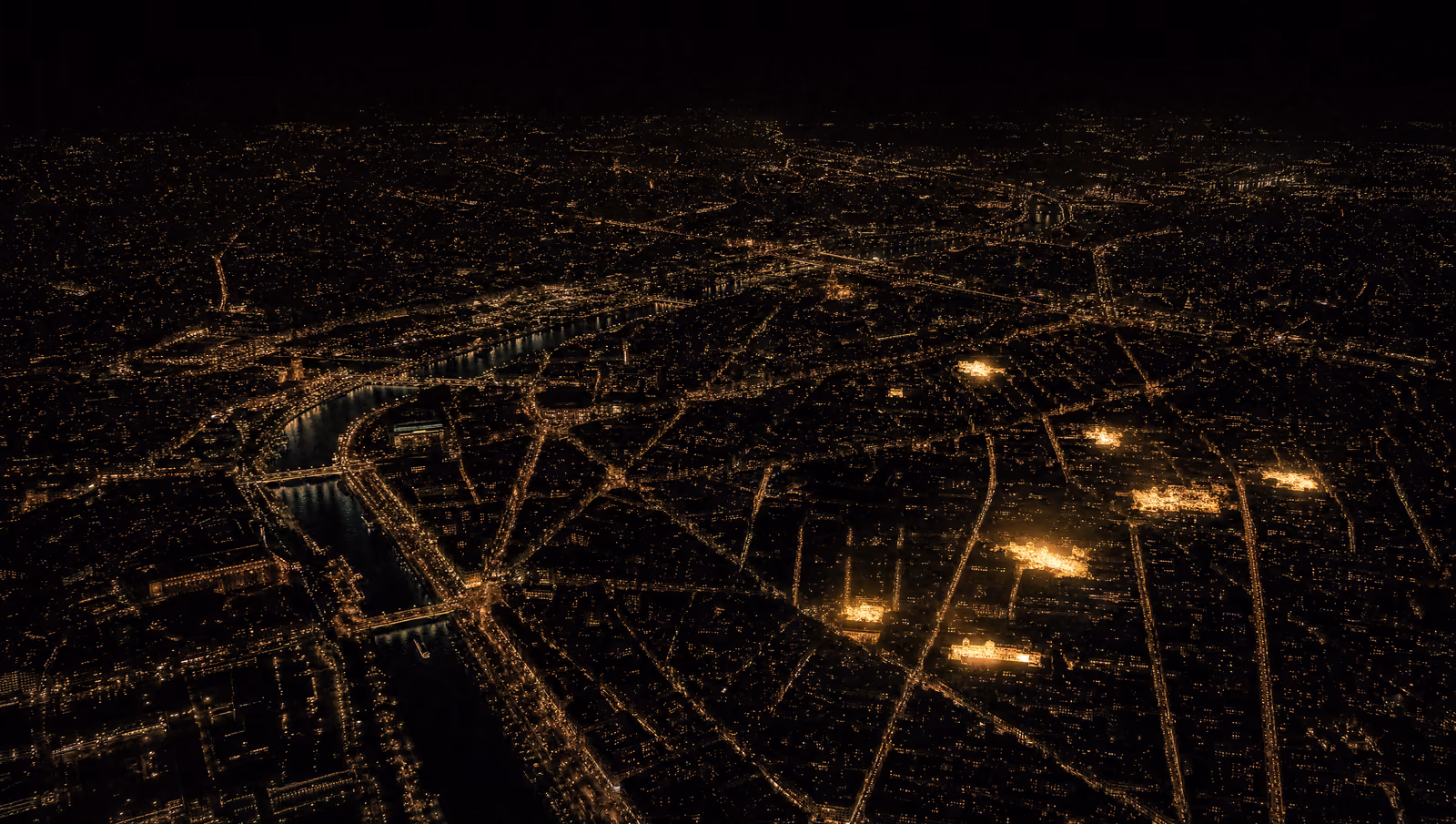 Vista aérea de París de noche: el Sena atraviesa la ciudad y algunas manzanas del este brillan más que el resto del tejido urbano.